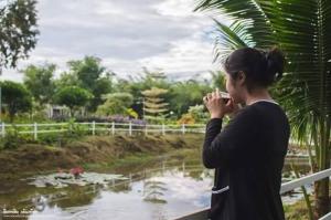 une femme parlant sur un téléphone portable devant un étang dans l'établissement Nonplern Garden Home Khaoyai, à Ban Noen Hom