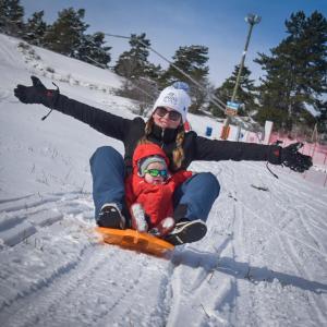 a woman sitting in the snow with a child on a snowboard at "La Combe Fleurie" Appartements & Chambres in Saint-Bonnet-en-Champsaur