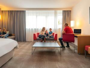a family sitting in chairs in a hotel room at Novotel Roissy Saint Witz in Saint-Witz