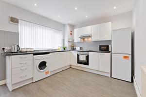 a kitchen with white cabinets and a washer and dryer at Alma Accommodation - TV in Every Bedroom! in Swansea