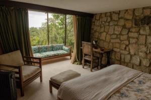 a bedroom with a stone wall and a bed and a window at Posada del Páramo - RNSC Bosque de niebla in Guasca