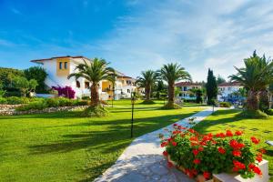 a park with red flowers and palm trees and houses at Chrousso Village in Paliouri