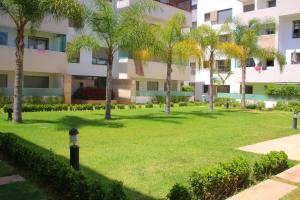 a park in front of a building with palm trees at Appartement dans résidence Paradis Beach in Mohammedia