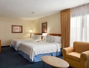 a hotel room with two beds and a chair at Suburban Studios in Fort Wayne