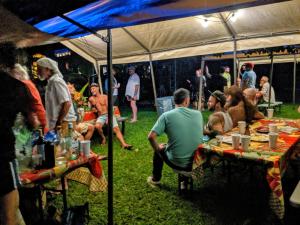 grupa ludzi siedzących przy stolikach pod namiotem w obiekcie Kehena Mauka Nui Club LGBTQIA+ Clothing Optional w mieście Pahoa
