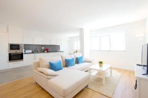 a white living room with a white couch and blue pillows at Penthouse with rooftop pool - Duna Parque Group in Vila Nova de Milfontes