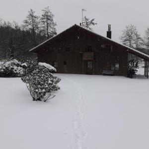 ein schneebedecktes Haus mit einem Gebäude im Hintergrund in der Unterkunft Le Grand Chalet in La Chapelle