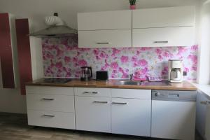 una cocina con armarios blancos y papel pintado de flores rosas en Ferienwohnung Fröhlich en Dorfprozelten
