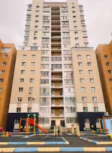 un gran edificio de apartamentos con un parque infantil delante de él en Трехкомнатные апартаменты в центре Левого Берега г.Нур-султан en Astaná