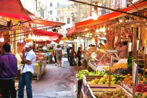 un grupo de personas caminando por un mercado con frutas y hortalizas en Perla del Borgo, en Palermo