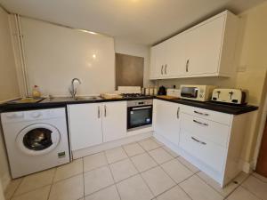 a kitchen with white cabinets and a washing machine at Charming Cottage style 3 bedroom property in Merthyr Tydfil