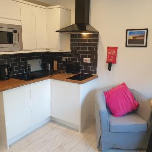 a kitchen with white cabinets and a blue chair with a pink pillow at Sweet Suites Residence in Lytham St Annes