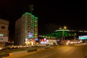 een hoog gebouw met groene lichten 's nachts bij العييري للوحدات المفروشة الباحة 1 in Al Baha