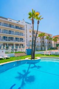 a swimming pool with a palm tree in front of a hotel at Hotel Sur in Cala Bona