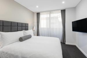 1 dormitorio con 1 cama blanca y TV de pantalla plana en Meriton Suites North Sydney en Sídney