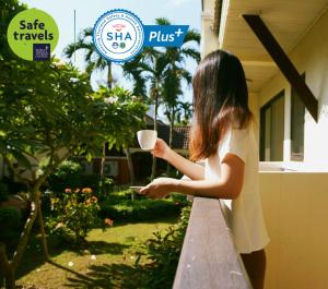 Eine Frau, die auf einem Balkon steht und eine Tasse Kaffee hält. in der Unterkunft Luckswan Resort Chiang Rai - SHA Extra Plus in Chiang Rai