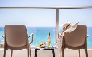 Ramada Hotel & Suites by Wyndham Netanya في نتانيا: امرأة تجلس على كرسي مع زجاجة من النبيذ