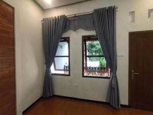 Cette chambre dispose de deux fenêtres avec des rideaux bleus. dans l'établissement Mudhia Homestay, à Magelang