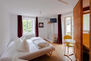 1 dormitorio con cama blanca, silla y ventana en Hotel Vallatscha, en Curaglia