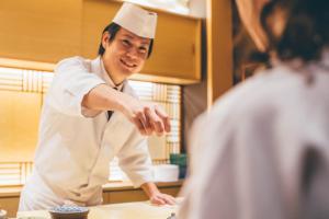 a man in a chef hat pointing at a table at 宿坊 観音院 Temple Hotel Kannonin in Kiryu