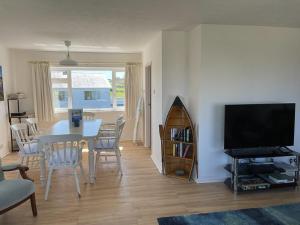 a living room with a dining table and a television at Deu Draeth in Abersoch