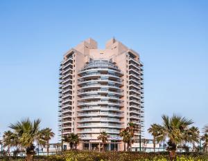 內坦亞的住宿－Ramada Hotel & Suites by Wyndham Netanya，一座高大的建筑,前面有棕榈树