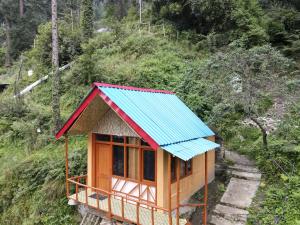 a small house with a blue roof on a hill at Reverberate Cafe & Cottages - Negi's Place in Jibhi