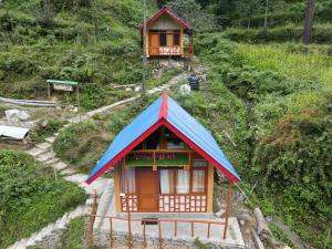 a small building with a blue roof on a hill at Reverberate Cafe & Cottages - Negi's Place in Jibhi
