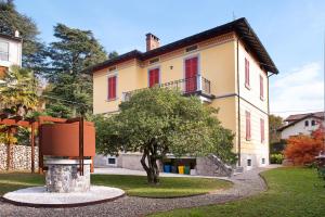 une grande maison jaune avec un arbre en face dans l'établissement Casa Corten Mountain Lago Maggiore, à Laveno-Mombello