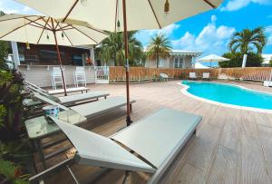 eine Terrasse mit Stühlen und Sonnenschirmen neben einem Pool in der Unterkunft Ti Verger in Sainte-Luce