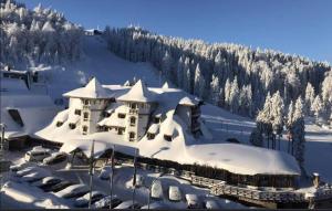 a building covered in snow with cars parked in front at Privatni apartman U532 - u sklopu hotela Vučko Jahorina in Jahorina