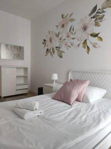 białe łóżko z różowymi poduszkami i obrazem kwiatowym na ścianie w obiekcie Lovely Apartment vis-a-vis Medicover and Paley Institute w Warszawie