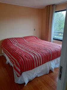 a bedroom with a bed with a red comforter and a window at Departamento Temuco Thiers in Temuco