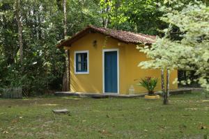 una pequeña casa amarilla con una puerta azul en un patio en Sítio Pássaro Ímpar - Para pousar e repousar, en Curuçá