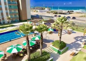 a resort with a pool and palm trees and umbrellas at VG FUN-OCEAN VIEW BEACH FRONT APARTMENT-Fortaleza in Fortaleza