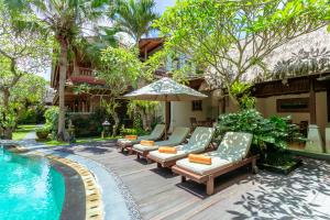 un patio con sillas y una sombrilla junto a la piscina en Lumbung Sari Ubud Hotel - CHSE Certified, en Ubud