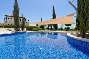 una piscina con una sombrilla y árboles en Ground floor apartment with golf and sea views - Roudias, Aphrodite Hills Resort en Kouklia