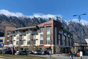 um hotel com montanhas ao fundo com carros estacionados em frente em Ramada Suites by Wyndham Queenstown Remarkables Park em Queenstown