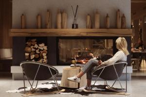 a woman sitting in chairs in front of a fireplace at Hotel Bohinj in Bohinj