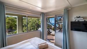 a bedroom with a bed and a tv and windows at Beach Music in Jeffreys Bay