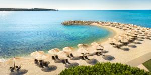 eine Gruppe von Sonnenschirmen und Stühlen am Strand in der Unterkunft Aminess Maestral Hotel in Novigrad Istria