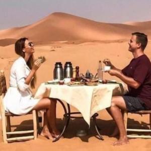 a man and woman sitting at a table in the desert at Berber Soul luxury Camp in Merzouga