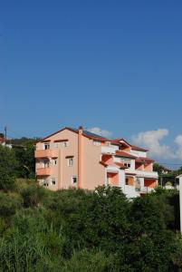 un bâtiment rose sur une colline avec des buissons dans l'établissement Apartments Toska, à Rab