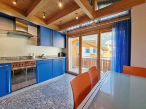 a kitchen with blue cabinets and a table with orange chairs at Snowfun B Penthouse in Saas-Fee