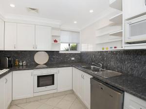 Una cocina blanca con gabinetes blancos y un fregadero. en Werrina Townhouse, en The Entrance