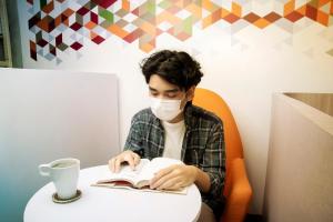 a man wearing a face mask reading a book at Tuju Arteri Pods in Jakarta