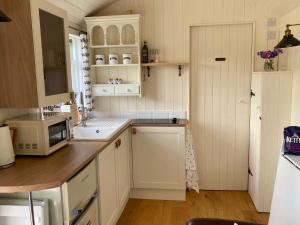 a kitchen with white cabinets and a sink and a microwave at Willow Brook Shepherd Hut in Sidmouth