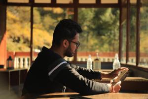 a man sitting at a table reading a book at Odin Hostel Shoja in Shoja