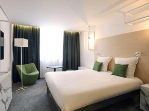 a hotel room with a large bed and a green chair at Mercure Nancy Centre Gare in Nancy