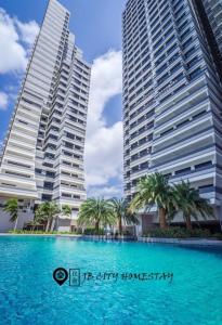 twee hoge gebouwen met palmbomen voor een zwembad bij Meridin Medini @ JB City Homestay in Johor Bahru
